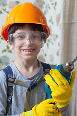 Image showing boy in a construction helmet and safety goggles with a drill in 