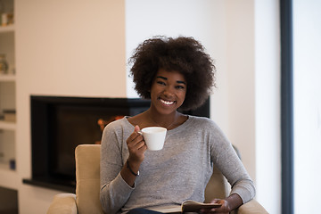 Image showing black woman reading book  in front of fireplace