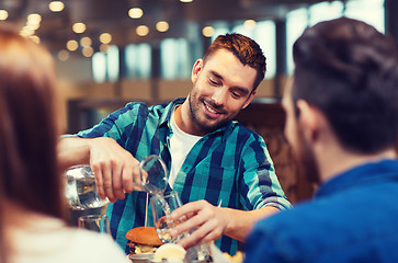 Image showing happy man with friends pouring water at restaurant