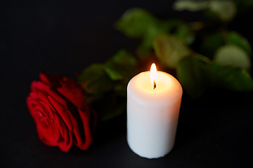 Image showing red rose and burning candle over black background