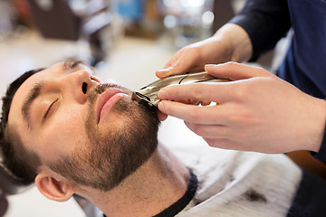 Image showing man and barber with trimmer cutting beard at salon