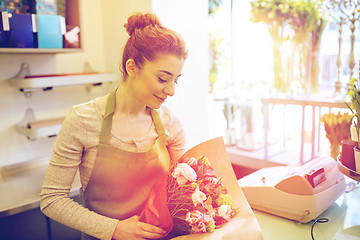 Image showing smiling florist woman packing bunch at flower shop