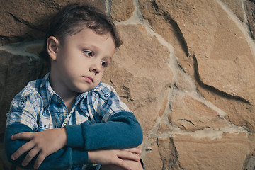 Image showing sad little boy sitting near the wall