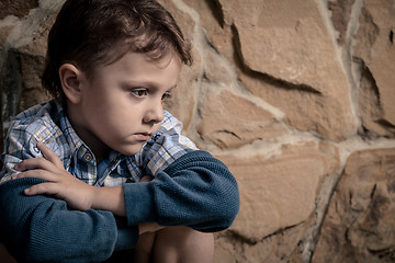 Image showing sad little boy sitting near the wall