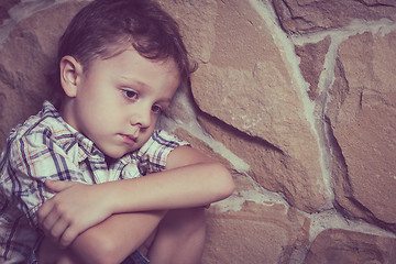 Image showing sad little boy sitting near the wall