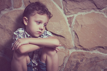 Image showing sad little boy sitting near the wall