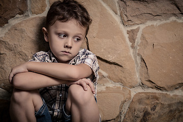 Image showing sad little boy sitting near the wall