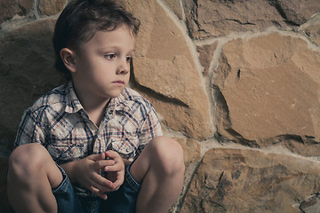 Image showing sad little boy sitting near the wall