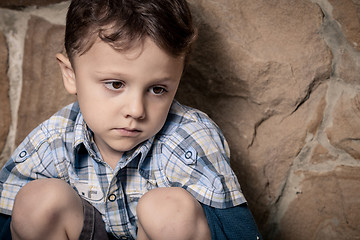 Image showing sad little boy sitting near the wall