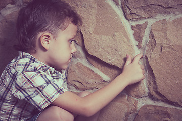 Image showing sad little boy sitting near the wall