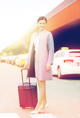 Image showing smiling young woman with travel bag over taxi