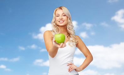 Image showing happy young woman with green apple over blue sky