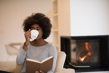 Image showing black woman reading book  in front of fireplace