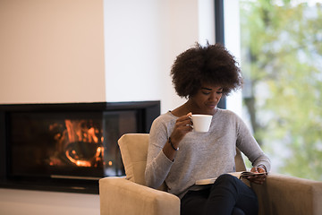 Image showing black woman reading book  in front of fireplace