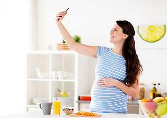 Image showing happy pregnant woman with smartphone at kitchen