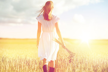 Image showing young woman with cereal spikelets walking on field