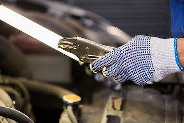 Image showing mechanic man with pliers repairing car at workshop