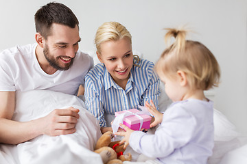 Image showing happy family with gift box in bed at home