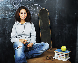 Image showing young cute teenage girl in classroom at blackboard seating on ta