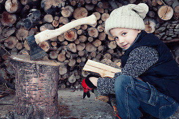 Image showing Little boy chopping firewood in the front yard at the day time.