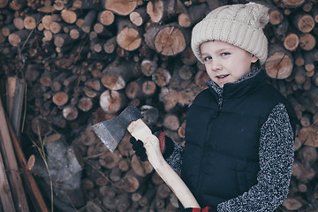 Image showing Little boy chopping firewood in the front yard at the day time.