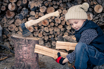 Image showing Little boy chopping firewood in the front yard at the day time.