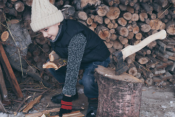 Image showing Little boy chopping firewood in the front yard at the day time.