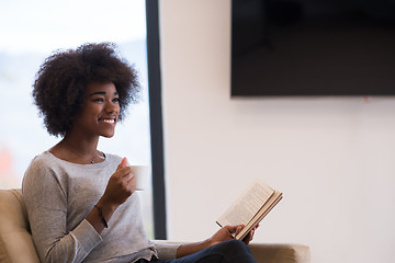 Image showing black woman reading book  in front of fireplace