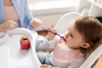 Image showing baby girl with spoon eating puree from jar at home