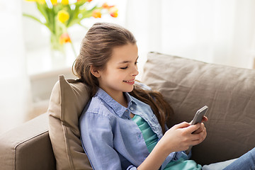 Image showing smiling girl texting on smartphone at home