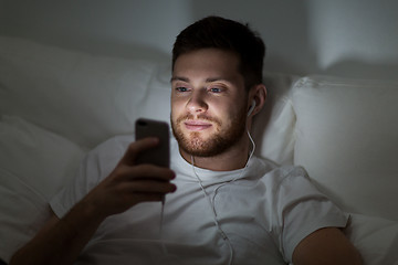 Image showing man with smartphone and earphones in bed at night