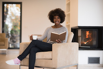 Image showing black woman reading book  in front of fireplace