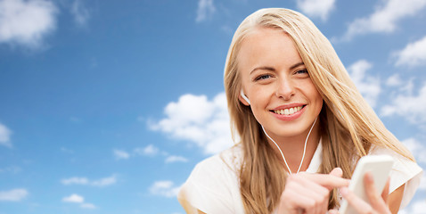 Image showing happy woman with smartphone and earphones over sky