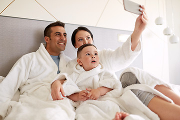 Image showing happy family with smartphone in bed at hotel room