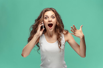 Image showing Shocked woman looking at mobile phone on green background