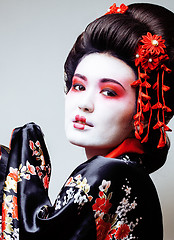 Image showing young pretty geisha in black kimono among sakura, asian ethno close up