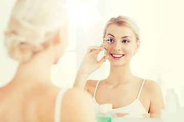 Image showing woman with curler curling eyelashes at bathroom