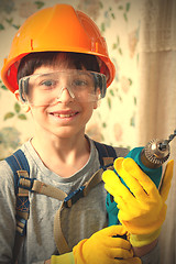 Image showing boy in a construction helmet and safety goggles with a drill in 