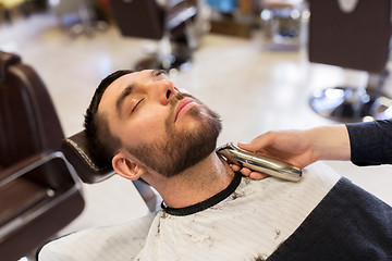 Image showing man and barber with trimmer cutting beard at salon