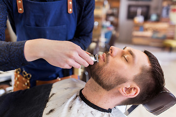 Image showing man and barber with trimmer cutting beard at salon