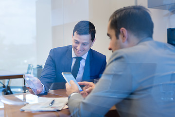 Image showing Two young businessmen using smart phones and touchpad at meeting.