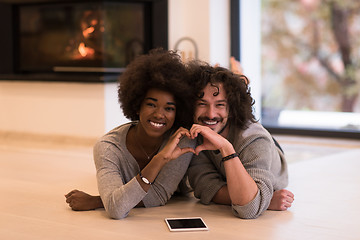 Image showing multiethnic couple showing a heart with their hands on the floor