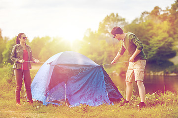 Image showing happy couple setting up tent outdoors