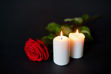 Image showing red rose and burning candles over black background