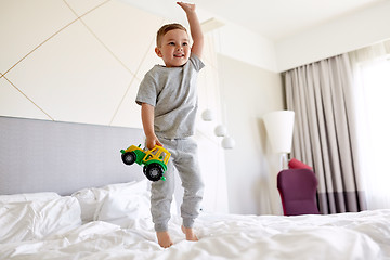 Image showing happy little boy with toy car on home or hotel bed