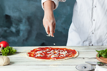 Image showing Closeup hand of chef baker in white uniform making pizza at kitchen