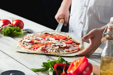 Image showing Closeup hand of chef baker in white uniform making pizza at kitchen