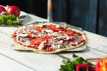 Image showing Closeup of a home made raw pizza with cheese and tomato sauce on a wooden background