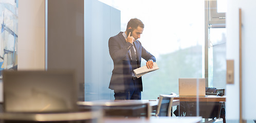 Image showing Businessman talking on mobile phone while looking at wristwatch.