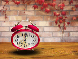 Image showing Old red alarm clock on wooden table In front of the brick wall